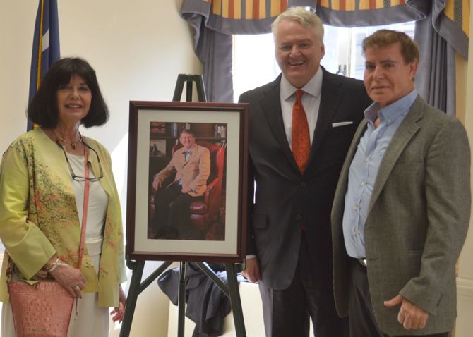 A photo of Deelane Reavis posed with State Treasurer Curtis Loftis and family friend Daniel Cartwright with a portrait of the late David Reavis.